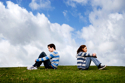 Teenage couple turned away from one another in field