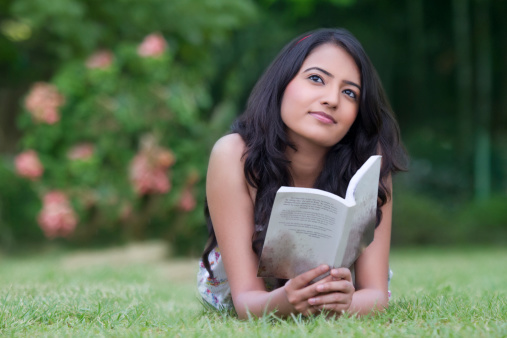 Thoughtful Indian woman with book relaxing in park